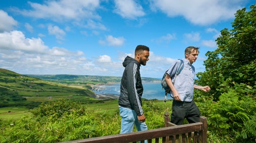 Two people walking on a coastal path with the beach and sea in the background at Ravenscar and Peak Alum Works, Yorkshire
